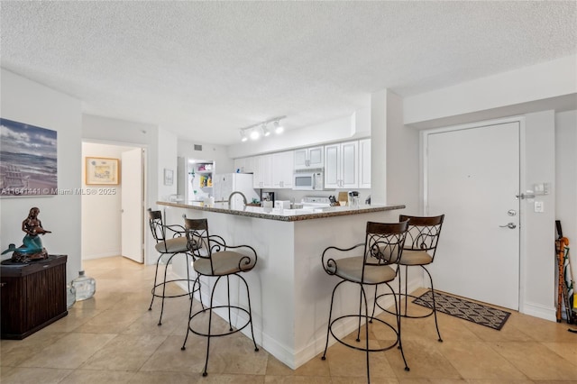 kitchen with a breakfast bar area, white cabinets, light stone countertops, white appliances, and a peninsula