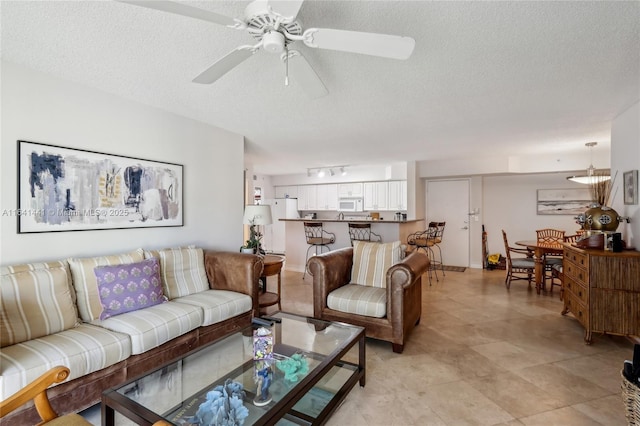 living room featuring a ceiling fan, rail lighting, and a textured ceiling