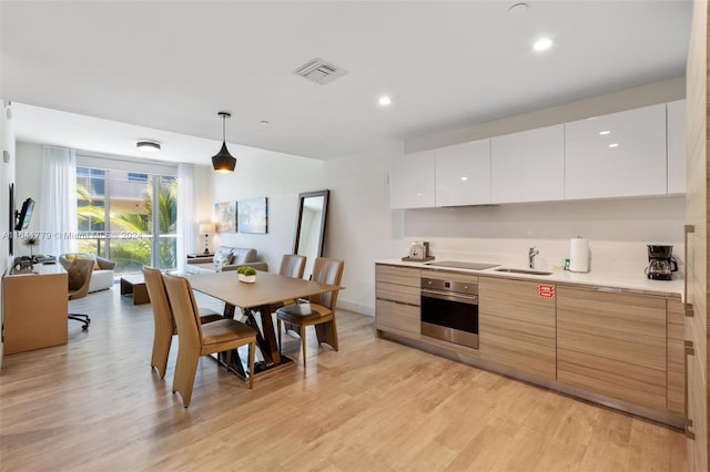 kitchen with pendant lighting, stainless steel oven, white cabinets, light hardwood / wood-style flooring, and light brown cabinetry