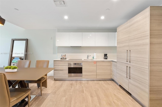 kitchen featuring stainless steel oven, sink, light brown cabinets, light hardwood / wood-style floors, and white cabinetry