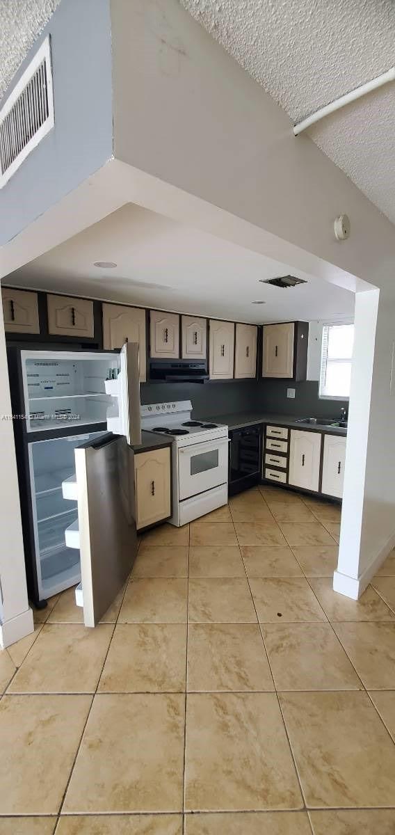 kitchen with ventilation hood, stainless steel fridge, white range with electric stovetop, light tile patterned flooring, and a textured ceiling