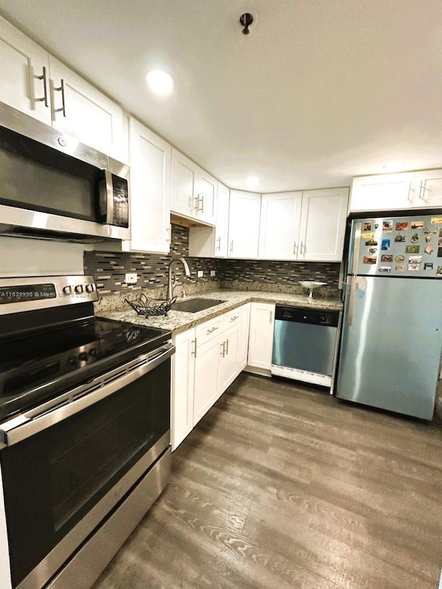 kitchen with appliances with stainless steel finishes, dark wood-type flooring, a sink, white cabinetry, and backsplash