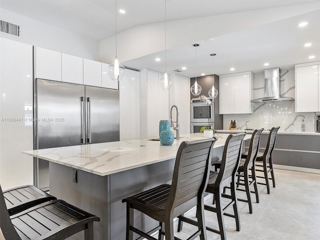 kitchen with a spacious island, wall chimney exhaust hood, a kitchen bar, hanging light fixtures, and white cabinets