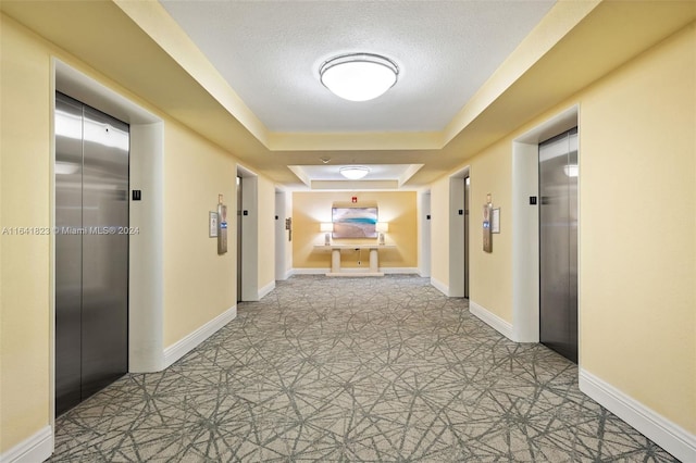 hallway with elevator, a textured ceiling, a tray ceiling, and light tile patterned floors