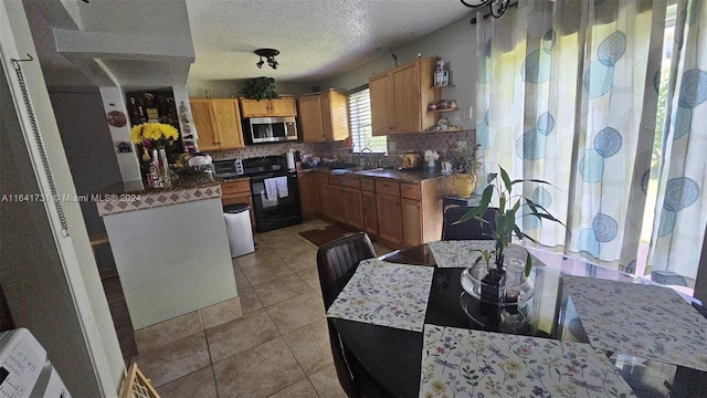 kitchen featuring a textured ceiling, light tile patterned floors, decorative backsplash, sink, and range