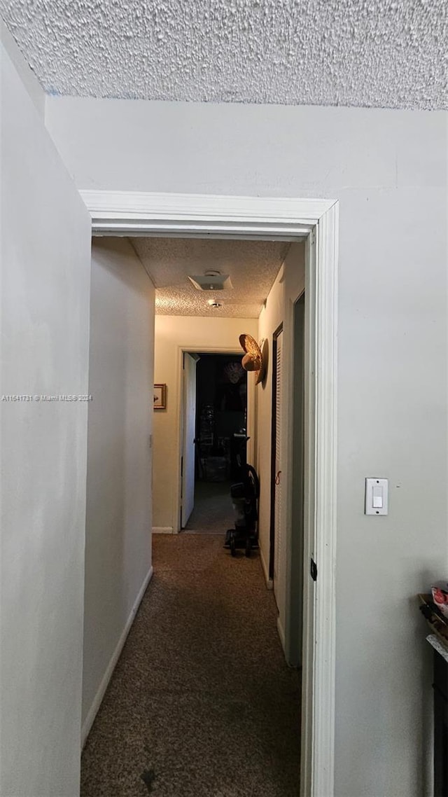 corridor featuring a textured ceiling and carpet flooring