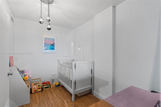 bedroom with light hardwood / wood-style floors, a crib, and a textured ceiling