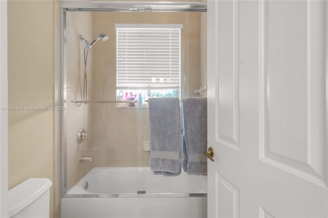 bathroom featuring combined bath / shower with glass door and toilet