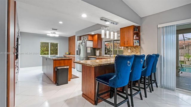 kitchen with vaulted ceiling, pendant lighting, backsplash, stainless steel fridge with ice dispenser, and kitchen peninsula