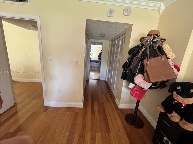 hallway with a textured ceiling, wood-type flooring, and crown molding