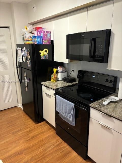 kitchen featuring black appliances, dark stone counters, white cabinetry, and light hardwood / wood-style floors