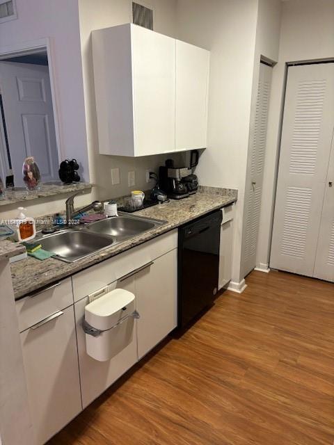 kitchen featuring light wood-style floors, black dishwasher, white cabinets, and a sink