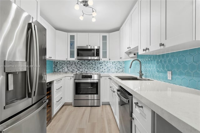 kitchen featuring appliances with stainless steel finishes, tasteful backsplash, sink, light stone counters, and light wood-type flooring