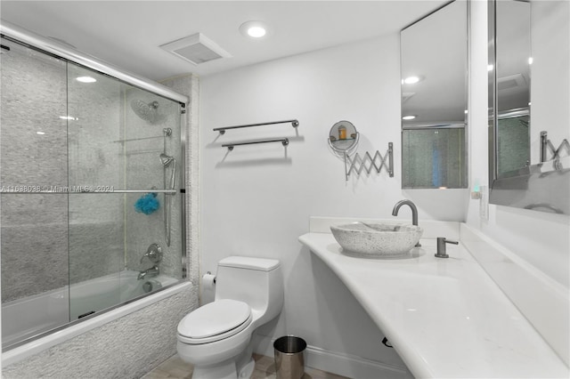 full bathroom featuring sink, shower / bath combination with glass door, toilet, and tile patterned flooring