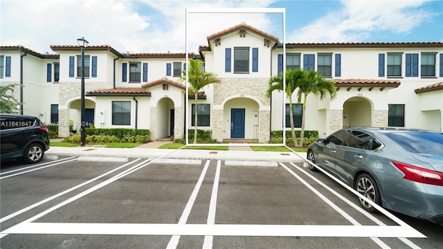 view of front of property featuring stucco siding, stone siding, uncovered parking, and a tile roof