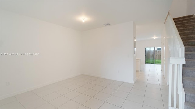 empty room featuring light tile patterned floors, stairway, baseboards, and visible vents