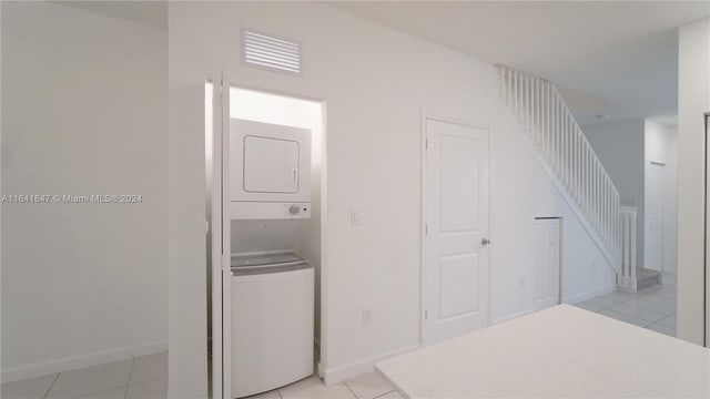 corridor with stairs, light tile patterned floors, baseboards, and stacked washing maching and dryer