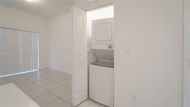 washroom featuring light tile patterned flooring, stacked washer / dryer, and laundry area