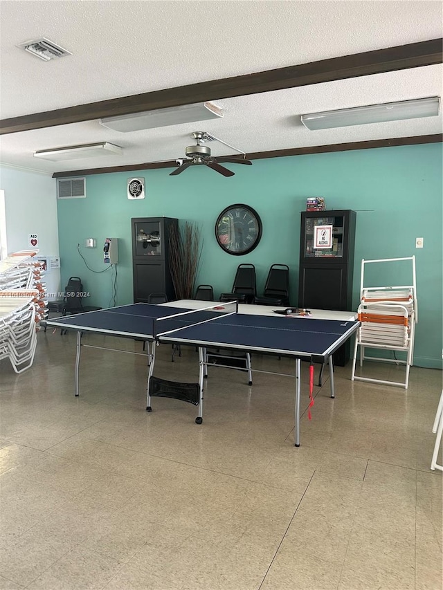 recreation room with ceiling fan, beamed ceiling, and a textured ceiling