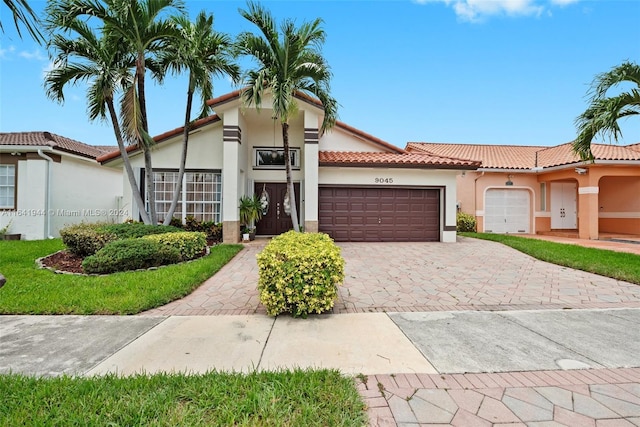 mediterranean / spanish house with a garage, a tiled roof, decorative driveway, and stucco siding