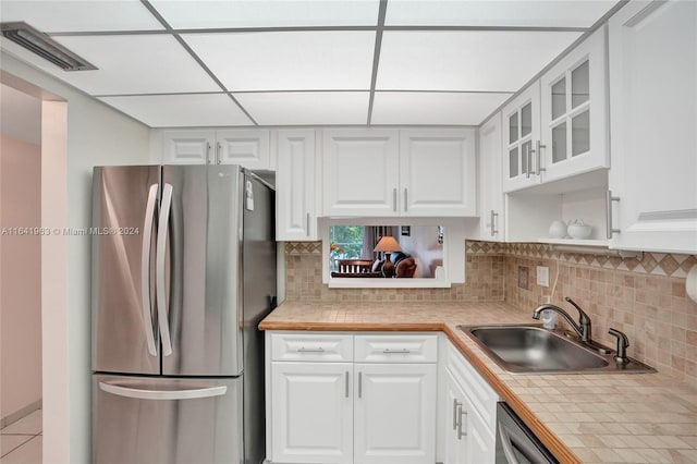 kitchen featuring backsplash, stainless steel appliances, white cabinetry, sink, and tile countertops