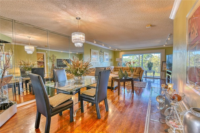 dining area with a textured ceiling, a notable chandelier, track lighting, and crown molding