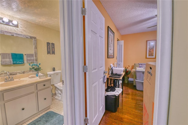 bathroom with hardwood / wood-style floors, a textured ceiling, vanity, and toilet