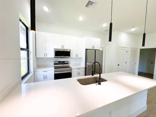 kitchen featuring appliances with stainless steel finishes, hanging light fixtures, sink, and white cabinetry