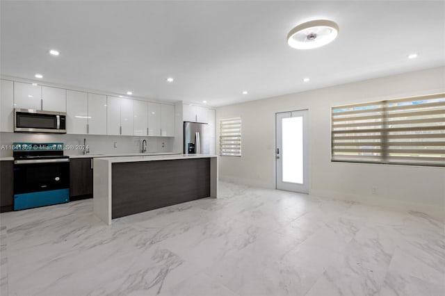 kitchen featuring light tile patterned flooring, appliances with stainless steel finishes, white cabinetry, a center island, and sink