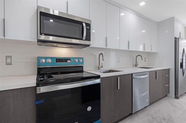 kitchen with light tile patterned floors, appliances with stainless steel finishes, sink, and white cabinets