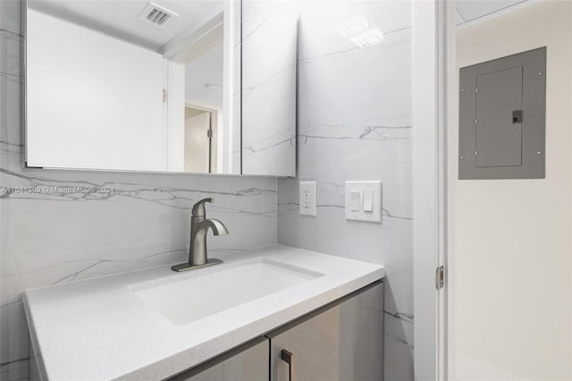 bathroom with visible vents, vanity, electric panel, and decorative backsplash