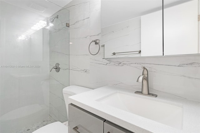 bathroom with tile walls, vanity, toilet, and a tile shower