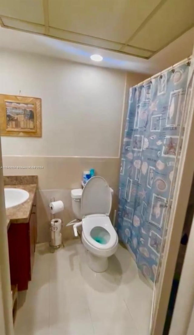 bathroom featuring a drop ceiling, walk in shower, tile patterned floors, toilet, and vanity