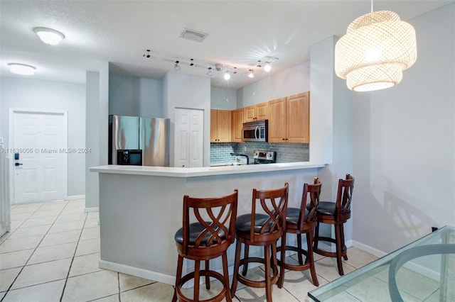 kitchen with a kitchen breakfast bar, tasteful backsplash, track lighting, decorative light fixtures, and stainless steel appliances