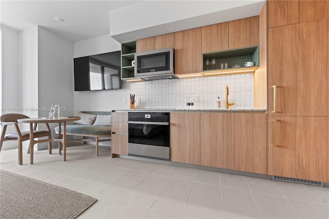 kitchen featuring backsplash, light stone counters, light tile patterned flooring, and oven