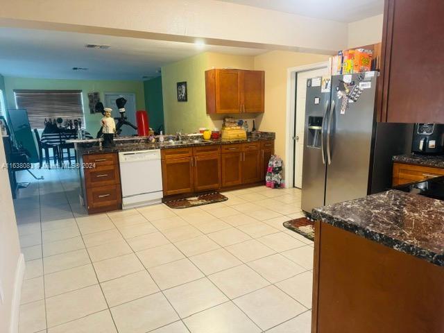 kitchen featuring stainless steel fridge with ice dispenser, dishwasher, light tile patterned flooring, dark stone counters, and kitchen peninsula