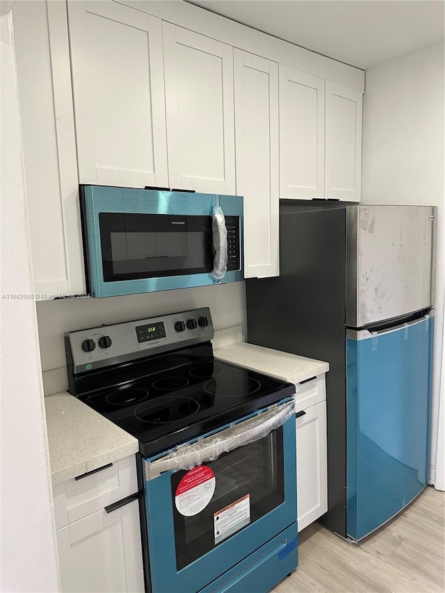 kitchen with light wood-type flooring, white cabinets, stainless steel appliances, and light stone countertops