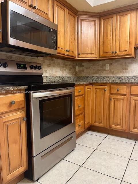 kitchen featuring appliances with stainless steel finishes, light tile patterned floors, backsplash, and dark stone counters