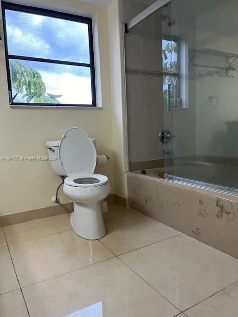 bathroom with tile patterned flooring, toilet, and combined bath / shower with glass door