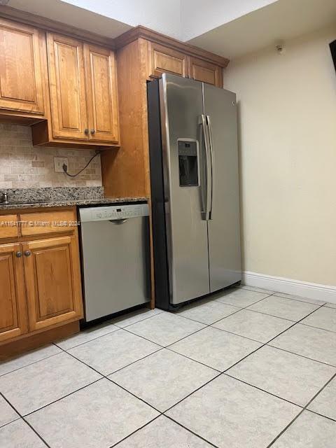 kitchen featuring stainless steel appliances, light tile patterned floors, backsplash, and dark stone counters