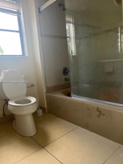 bathroom featuring combined bath / shower with glass door, toilet, and tile patterned floors