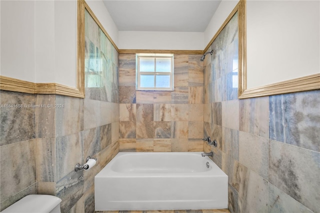 bathroom with toilet, tile walls, and tiled shower / bath combo