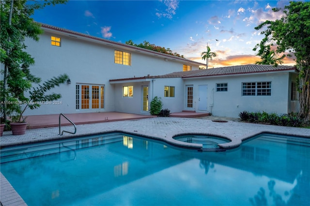 pool at dusk featuring an in ground hot tub, a patio area, and french doors