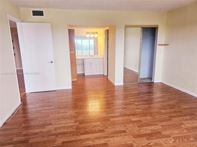 unfurnished bedroom featuring wood-type flooring, ensuite bathroom, and a closet