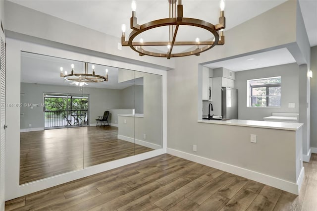 unfurnished living room with a notable chandelier, light wood-type flooring, sink, and plenty of natural light