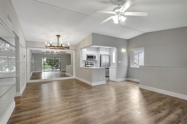 unfurnished living room with wood-type flooring, vaulted ceiling, ceiling fan with notable chandelier, and sink