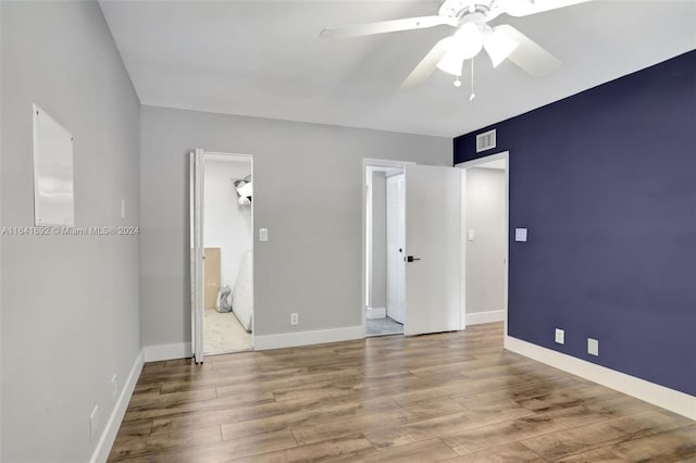 unfurnished bedroom featuring ensuite bath, hardwood / wood-style flooring, a walk in closet, and ceiling fan