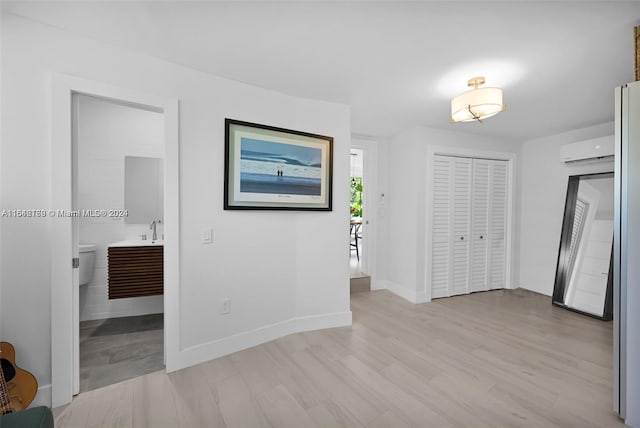 unfurnished bedroom featuring connected bathroom, light wood-type flooring, sink, and a wall unit AC