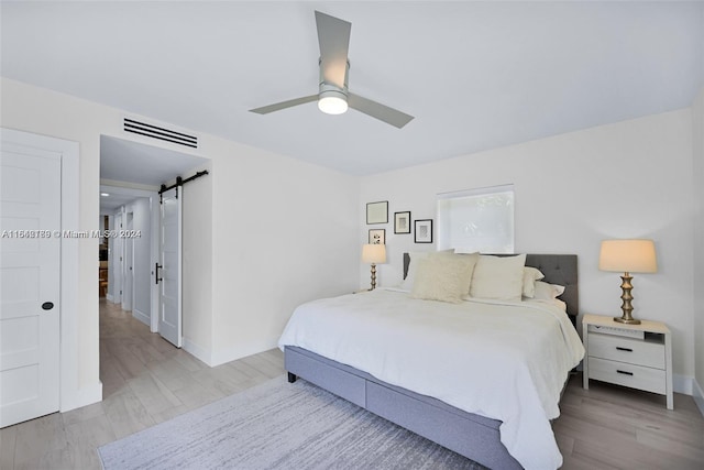 bedroom featuring ceiling fan, light hardwood / wood-style flooring, and a barn door