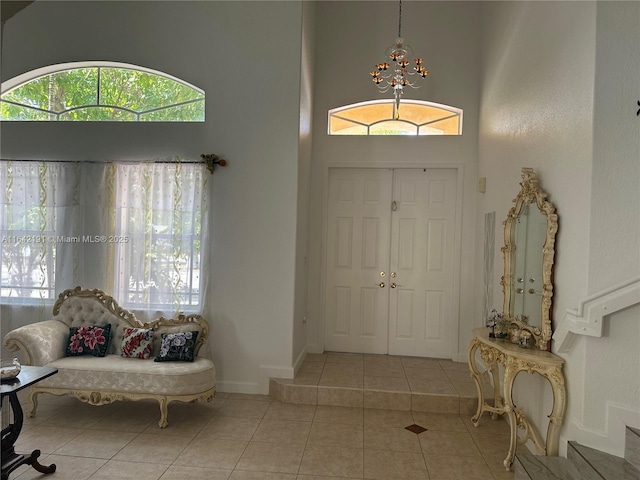 tiled entryway featuring baseboards, a towering ceiling, and a chandelier